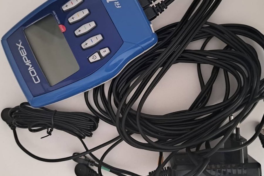 Boîtier bleu du Compex FIT 1.0 avec ses quatre câbles de connexion colorés et son chargeur secteur