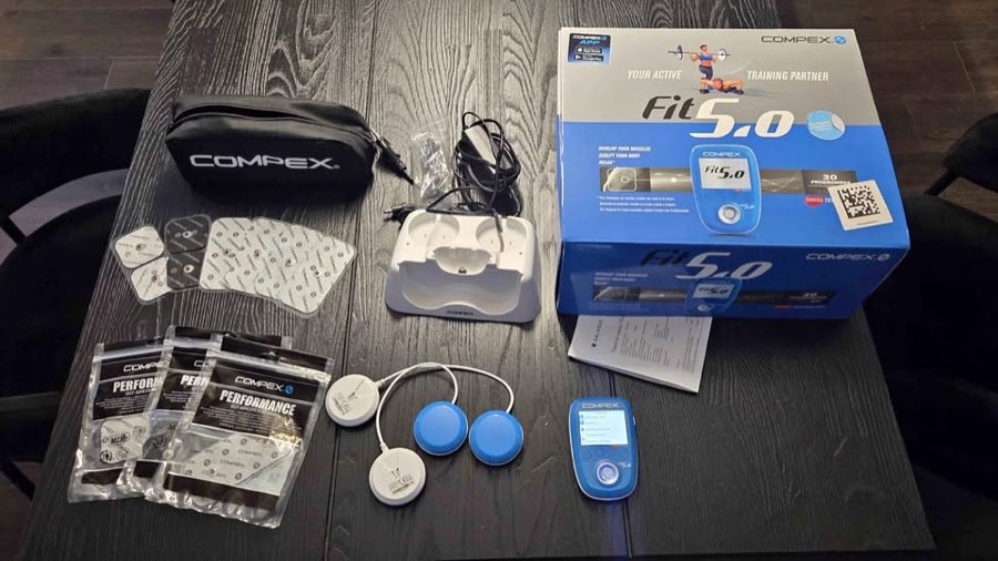 Contenu du coffret Compex FIT 5.0 : trousse, électrodes, chargeur, station de charge, deux modules sans fil et boîtier