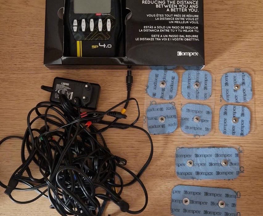 Contenu du coffret Compex SP 4.0 : boîtier dans sa boîte, chargeur, câbles et électrodes Snap carrées et rectangulaires