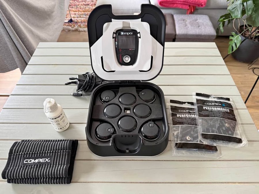 Mallette Compex SP 6.0 ouverte : boîtier à écran couleur, plateau de modules sans fil, sachets d'électrodes et gel conducteur
