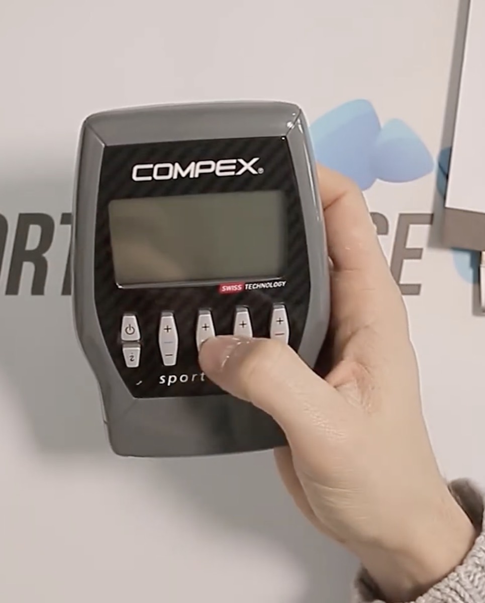 Boîtier du Compex Sport Elite tenu d'une seule main, écran monochrome et façade noire effet carbone