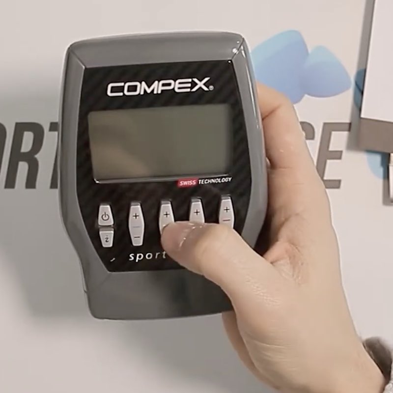 Boîtier du Compex Sport Elite tenu d'une seule main, écran monochrome et façade noire effet carbone