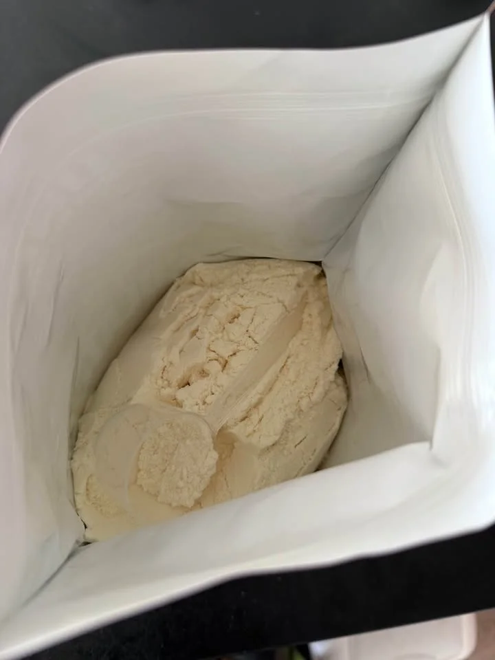 Poudre de la Pure Whey Isolate Squad Nutrition vanille et sa dosette, dans le sachet ouvert